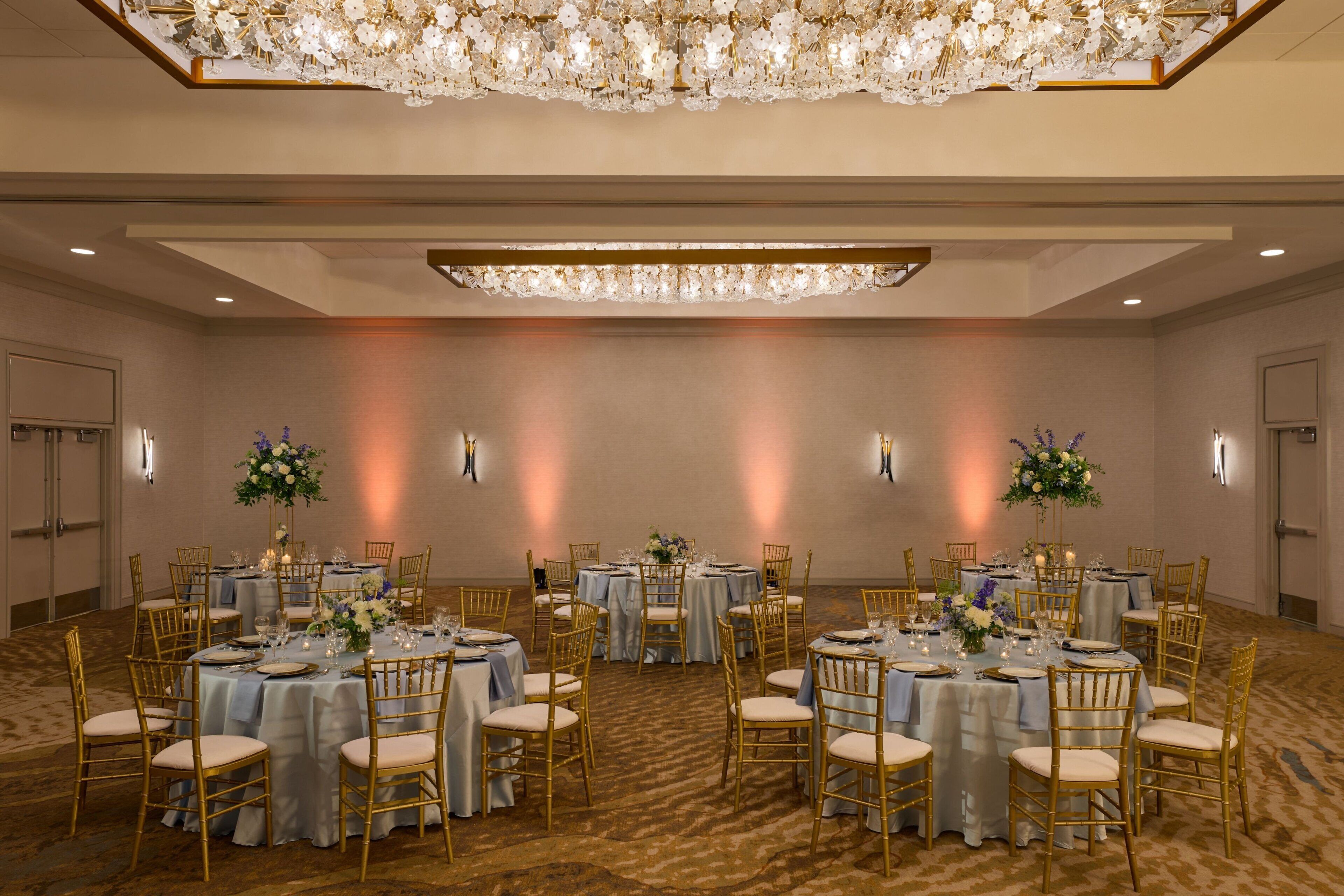 Un salón de banquetes con mesas redondas, sillas doradas y centros de mesa florales.