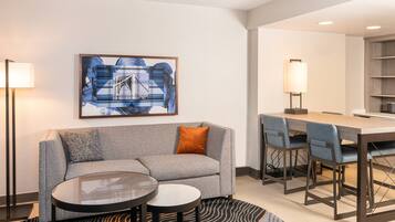 A modern living room with a grey sofa, a round coffee table, and a dining area with a long table and chairs.