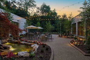 An outdoor patio area with tables and chairs, a small pond, and string lights. - Pittsburgh Airport Marriott (Coraopolis)