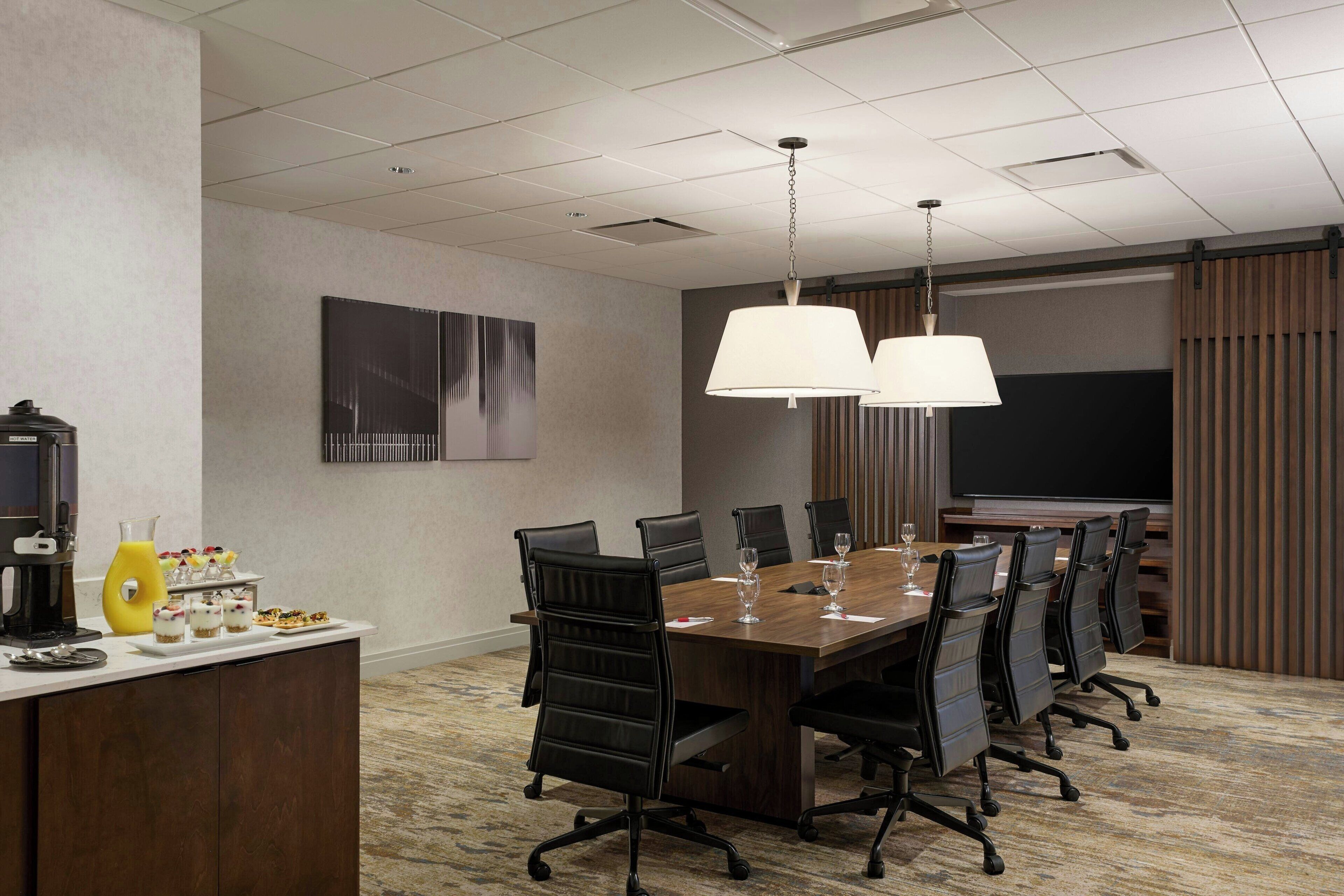 A conference room with a long table, black chairs, a projector screen, and a whiteboard.