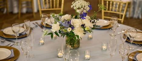 A table set for a formal event with white and gold tableware, clear glassware, and a centerpiece of white and blue flowers.