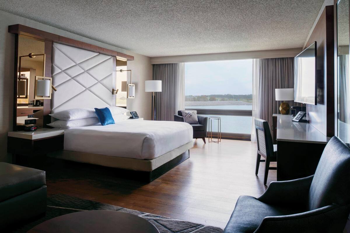 Ein Hotelzimmer mit einem großen Bett, einem Schreibtisch, einem Stuhl und Blick ins Freie.