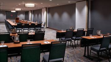 A conference room with multiple tables and chairs, a projector screen, and a presentation podium.