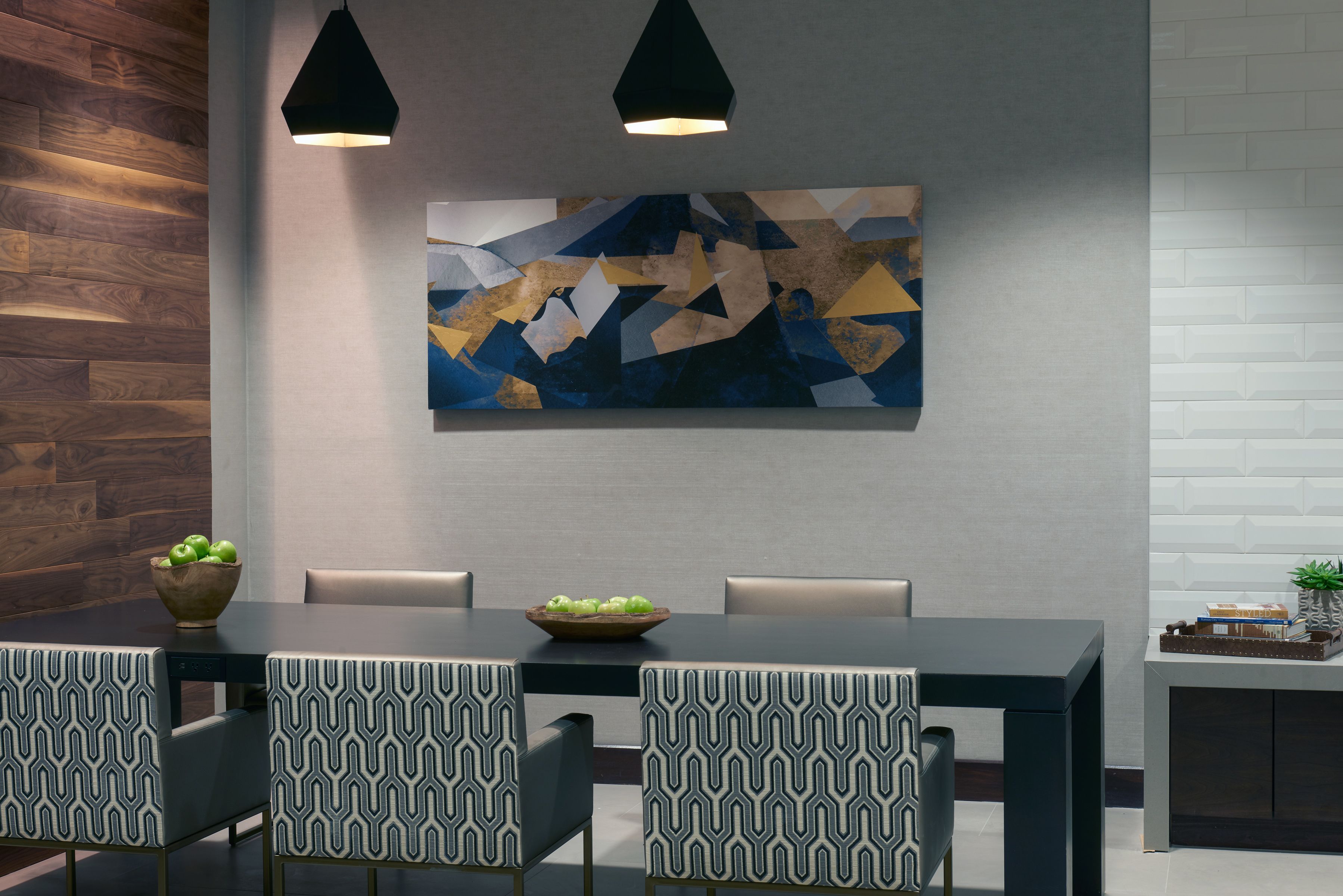 A modern dining area with a dark wooden accent wall, a geometric abstract painting, and a table with patterned chairs.