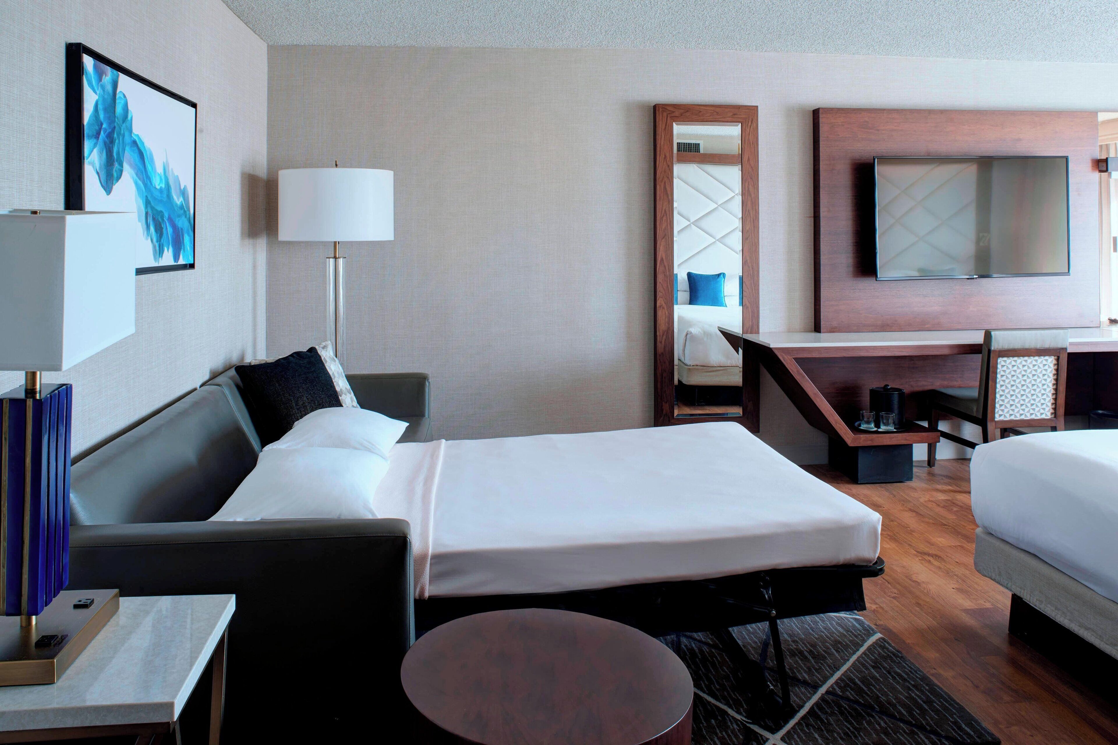 A hotel room with a bed, a desk, a chair, a TV, and a lamp.