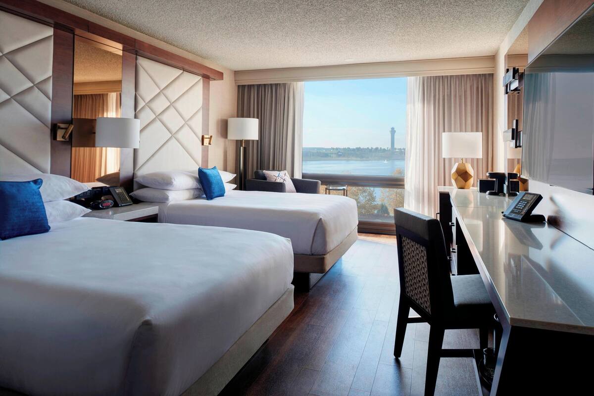 Ein Hotelzimmer mit zwei Betten, einem Schreibtisch und Blick auf ein Gewässer.