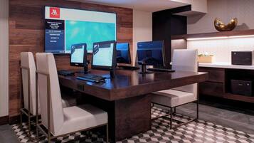 Un salón de conferencias de hotel moderno con un escritorio grande, múltiples monitores y asientos cómodos.