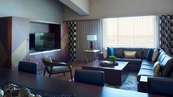 Una habitación de hotel moderna con un televisor de pantalla plana grande, un sofá, una mesa de centro y un comedor con una mesa y sillas de madera.