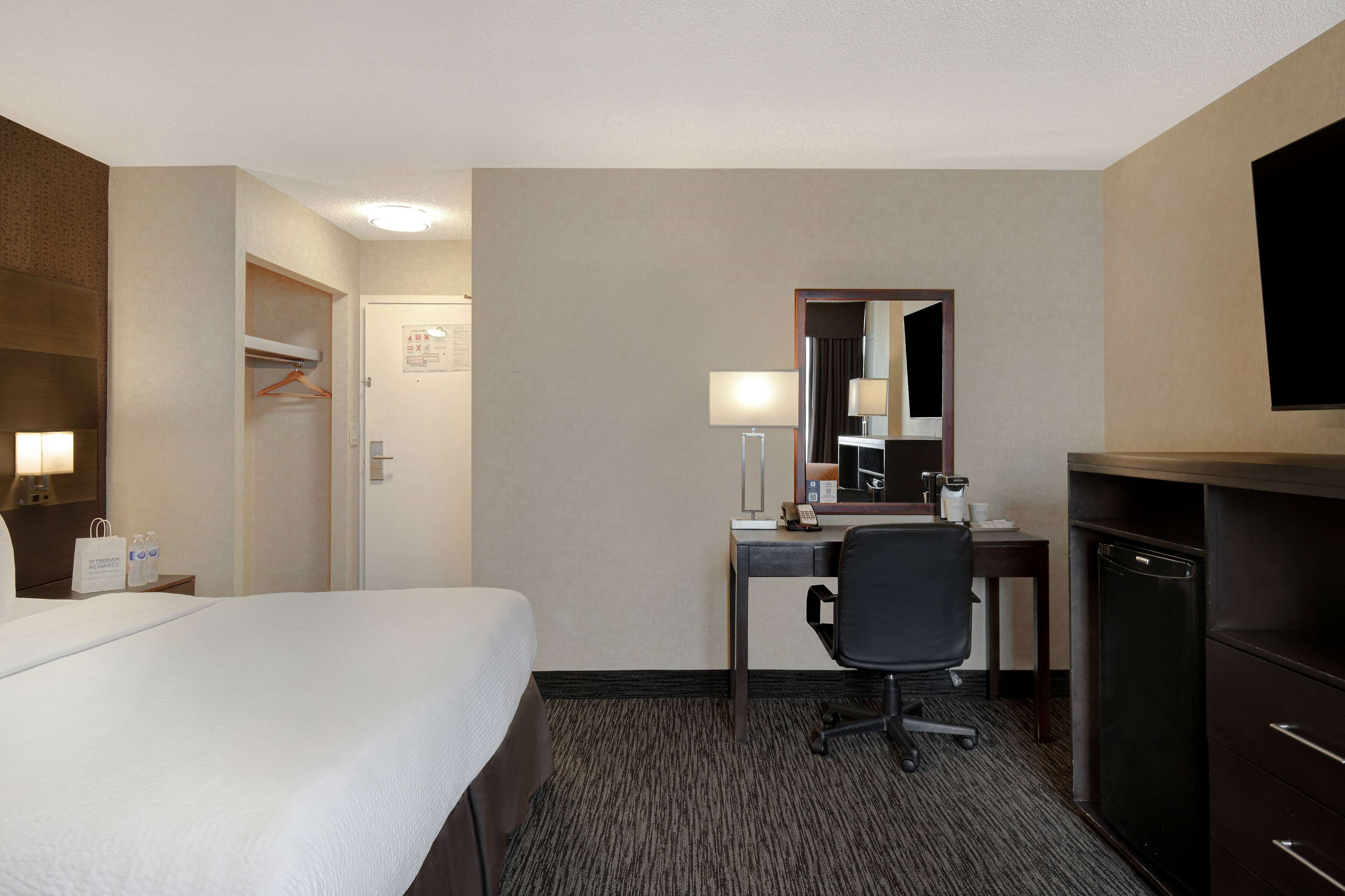 A hotel room with a bed, a desk with a chair, a mirror, a lamp, and a television.