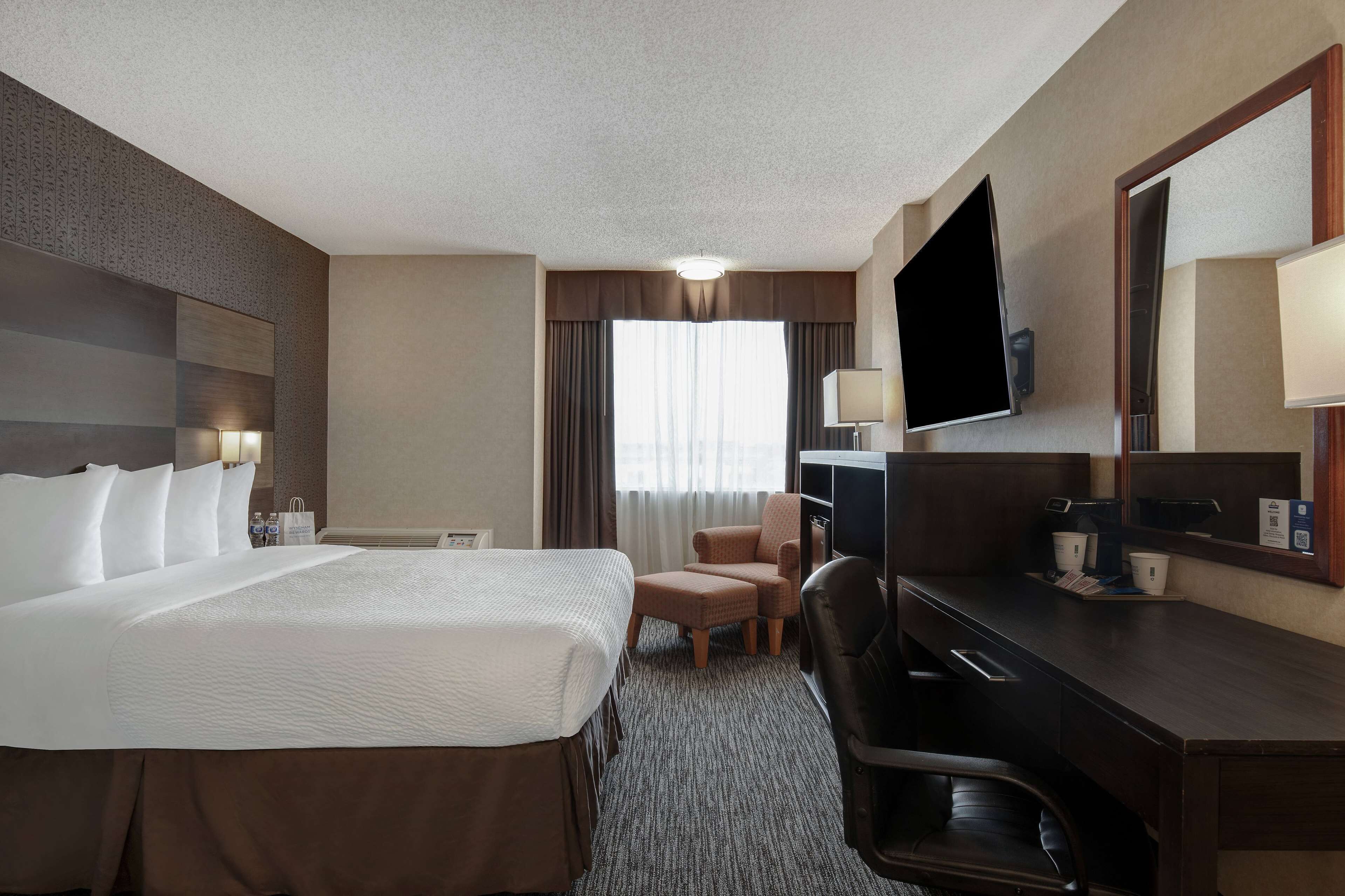 A hotel room with a large bed, a desk, a chair, a TV, and a window with curtains.