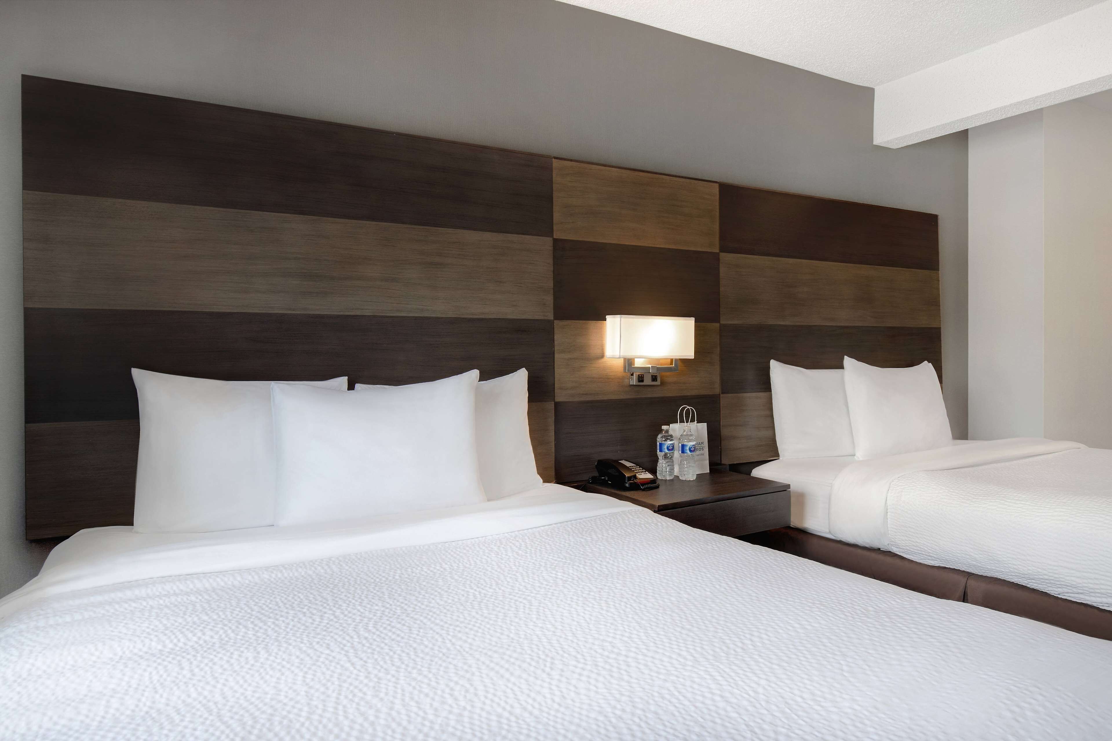 Habitación de hotel con dos camas, una mesita de noche con lámpara y teléfono en la pared.
