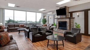 A spacious lounge area with leather sofas and armchairs, a fireplace, and large windows offering a city view. - Days Inn by Wyndham Calgary South (Calgary)