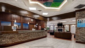 A reception area with a stone counter, wooden paneling, a clock, and a fireplace. - Days Inn by Wyndham Calgary South (Calgary)