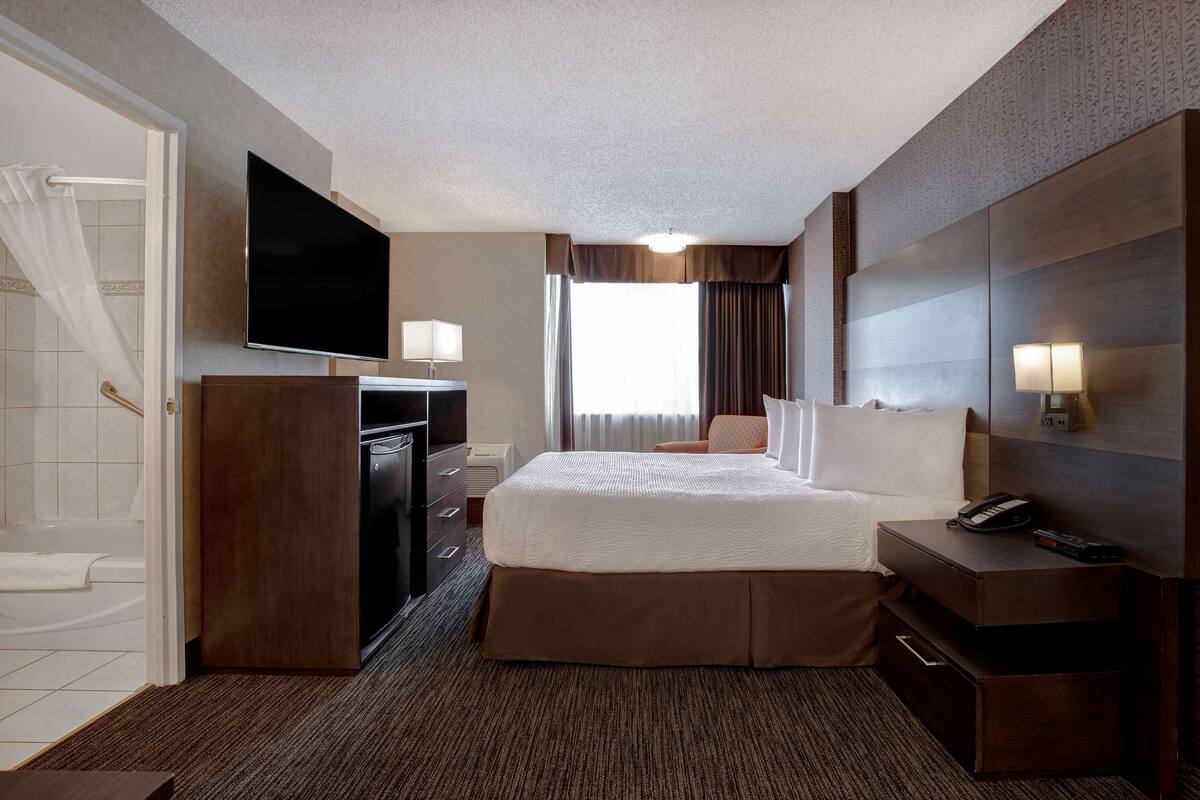 A hotel room with a large bed, a desk with a flat-screen TV, a dresser, and a bathroom with a shower and toilet.