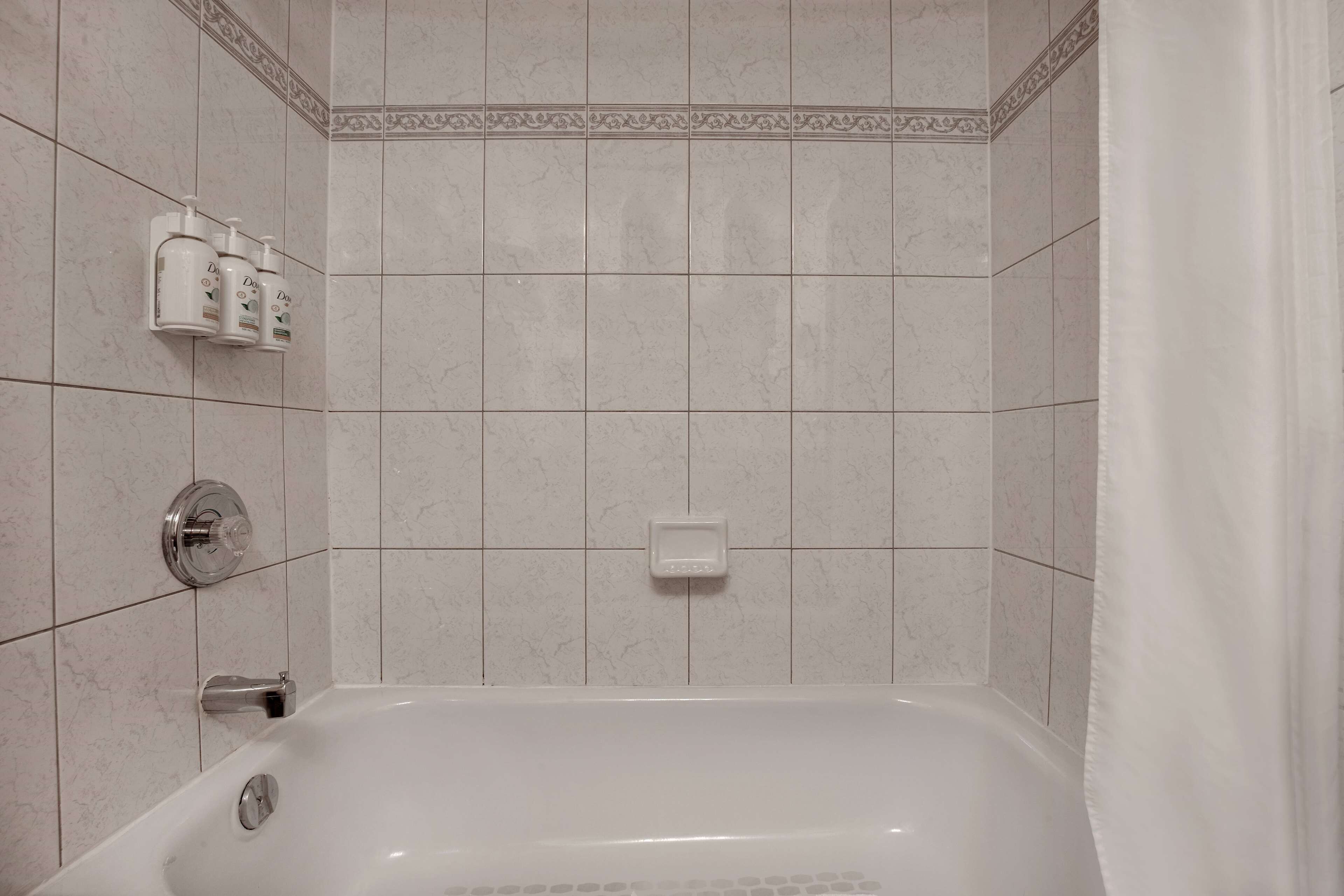 A bathroom with a bathtub, a hand soap dispenser, and a soap dish on the wall.