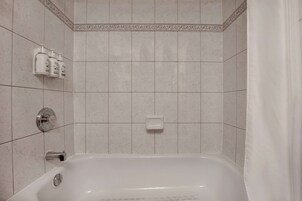 A bathroom with a bathtub, a hand soap dispenser, and a soap dish on the wall.