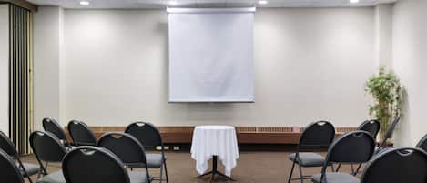 A conference room with rows of chairs, a projector screen, and a small table with a white cloth.