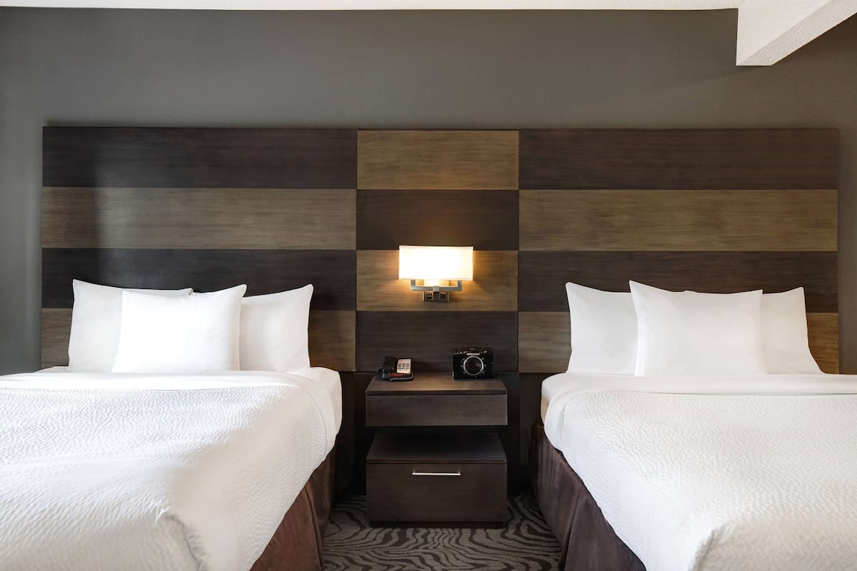 A hotel room with two beds, a nightstand with a lamp, and a camera.