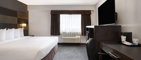 Quarto de hotel com cama, escrivaninha, cadeira, televisão, ar condicionado e cortinas.