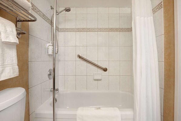 A bathroom with a bathtub, a shower with a handrail, a toilet, and a towel rack.