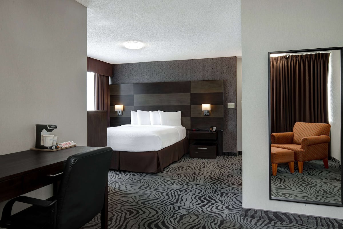 A hotel room with a bed, a desk, a chair, a nightstand, and a mirror.