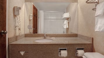 Un baño con lavamanos de encimera de granito, un espejo, un secador de pelo y un perchero para toallas.