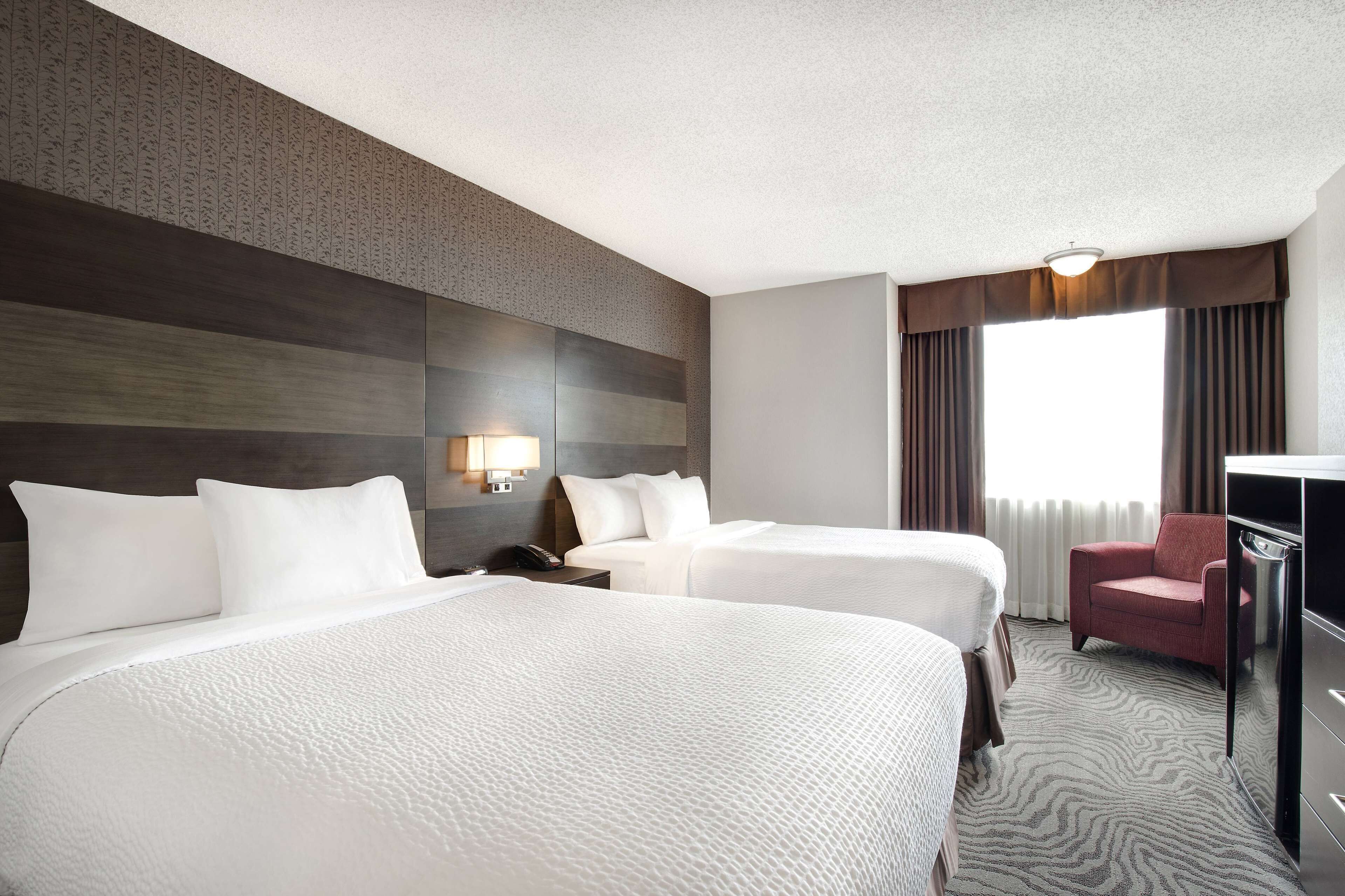A hotel room with two beds, a desk, a chair, and a large window with curtains.