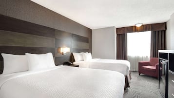 Quarto de hotel com duas camas, uma escrivaninha, uma cadeira e uma janela grande com cortinas.