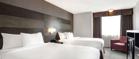 A hotel room with two beds, a desk, a chair, and a large window with curtains.