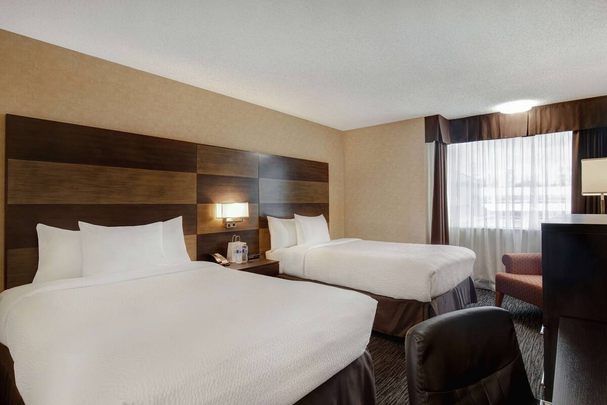 A hotel room with two beds, a desk, a chair, and a window with curtains.