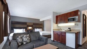 A hotel room with a bed, a sofa, a coffee table, a kitchenette with a microwave, and a refrigerator. - Days Inn by Wyndham Calgary South (Calgary)