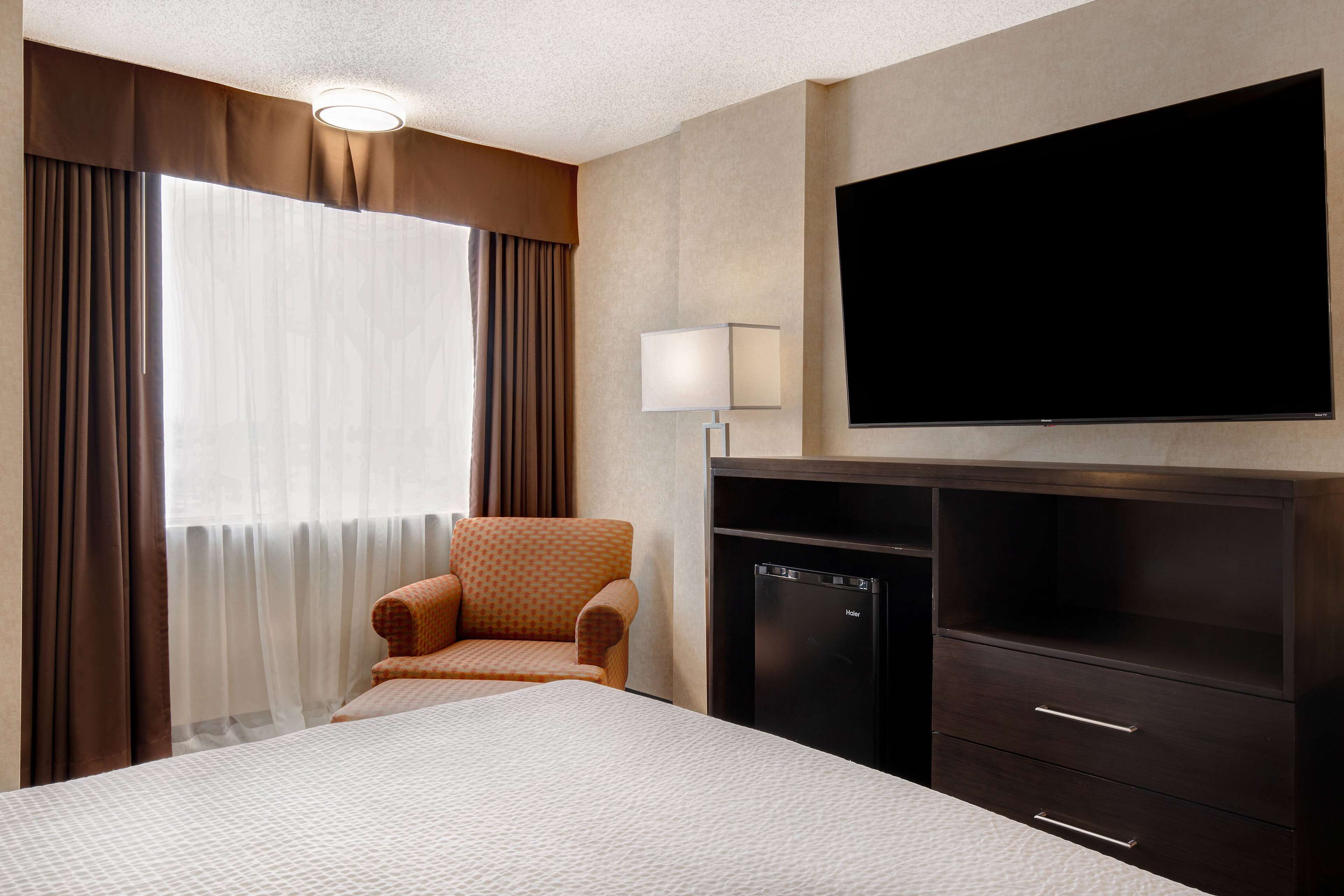 A hotel room with a bed, a chair, a television, and a minibar.