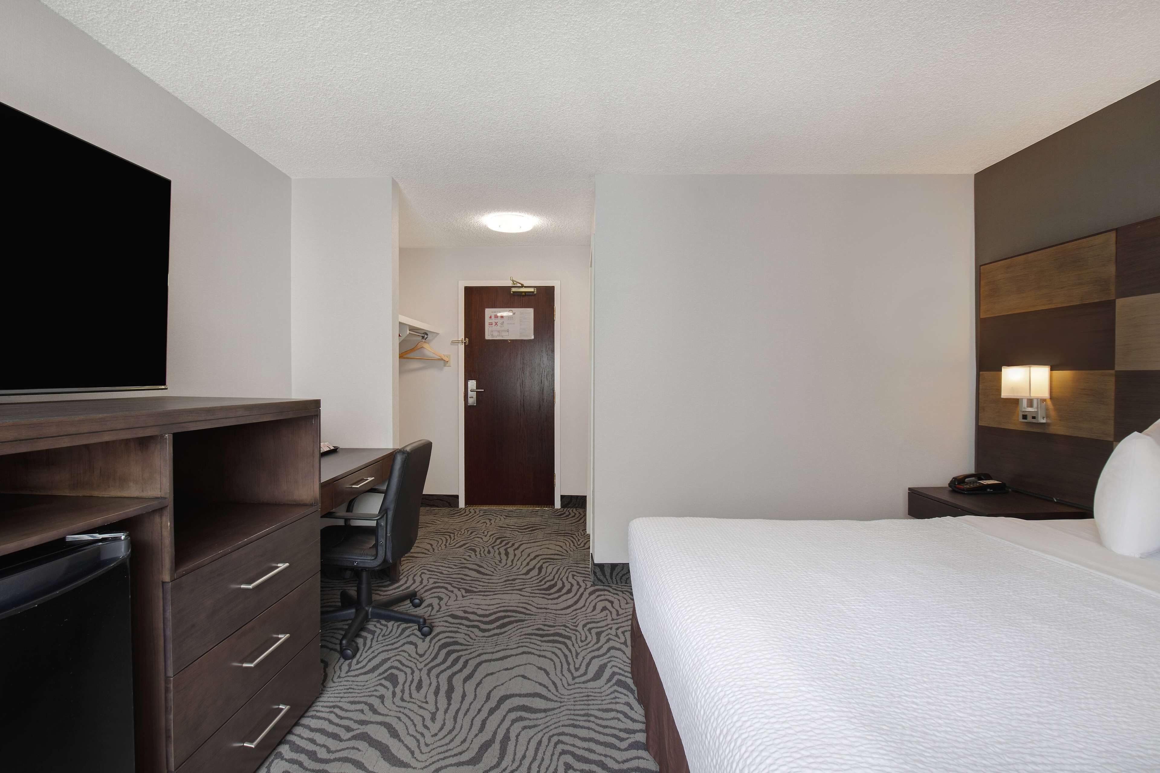 Een hotelkamer met een bed, een bureau met stoel, een televisietoestel en een kledingkast.