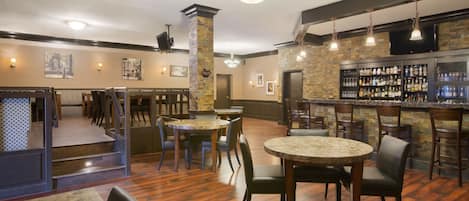 Un restaurante con suelo de madera, mesas redondas y sillas. Hay mostradores de bar con estantes llenos de botellas y vasos.