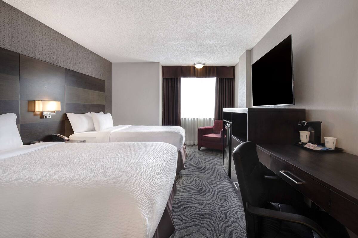 A hotel room with two beds, a desk, a chair, a TV, and a window with curtains.
