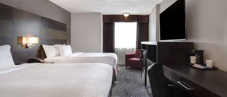 A hotel room with two beds, a desk, a chair, a TV, and a window with curtains.