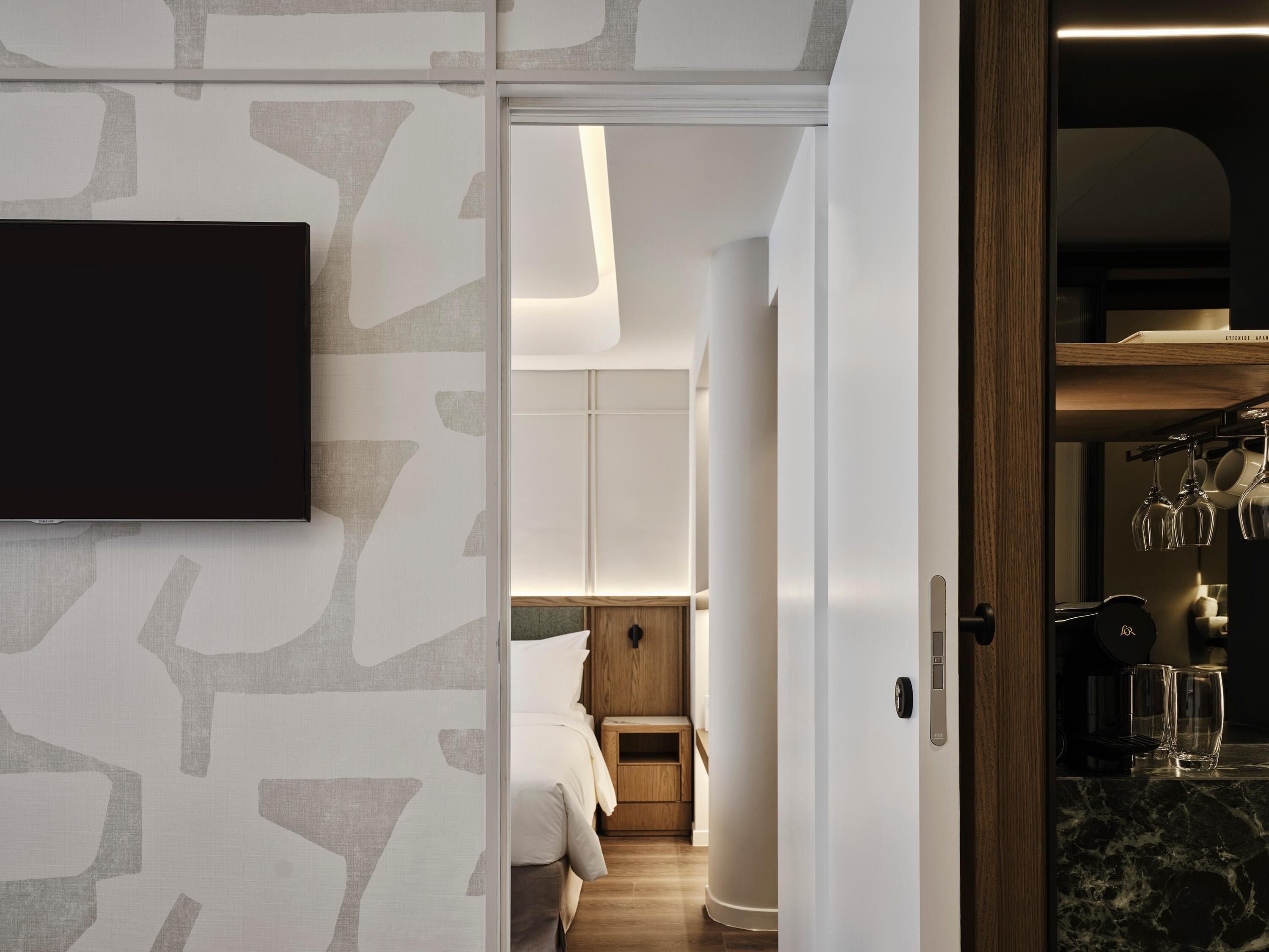 Une chambre d’hôtel moderne équipée d’un téléviseur à écran plat, d’un lit, d’une petite armoire en bois et d’un mini-bar.
