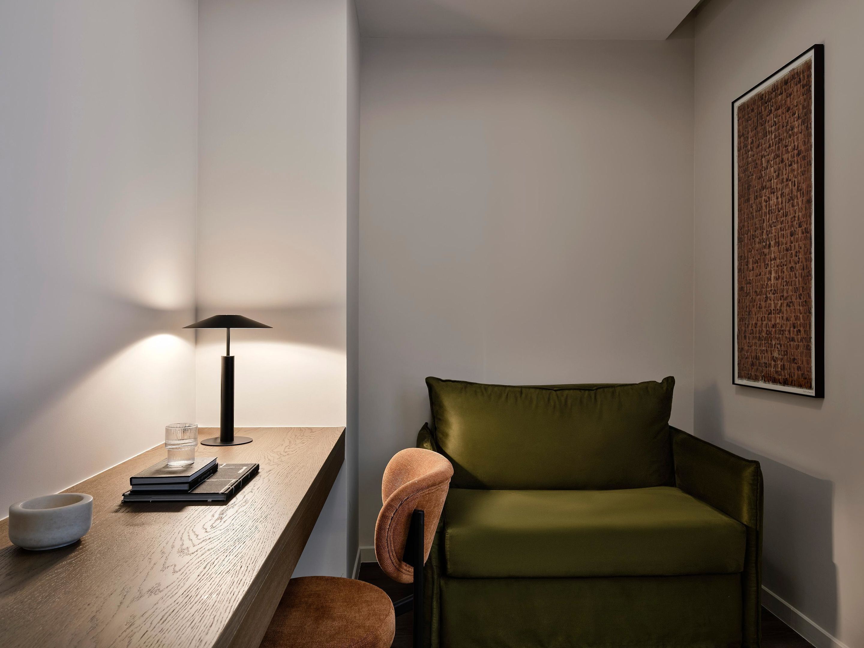 A modern room with a wooden desk, a green sofa, a lamp, and a framed artwork on the wall.