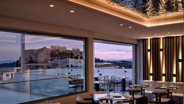 A restaurant with a view of a historic building and a body of water. Tables are set with plates, glasses, and cutlery.
