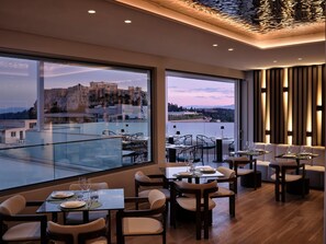A restaurant with a view of a historic building and a body of water. Tables are set with plates, glasses, and cutlery. - Electra Rhythm Athens (Athens)