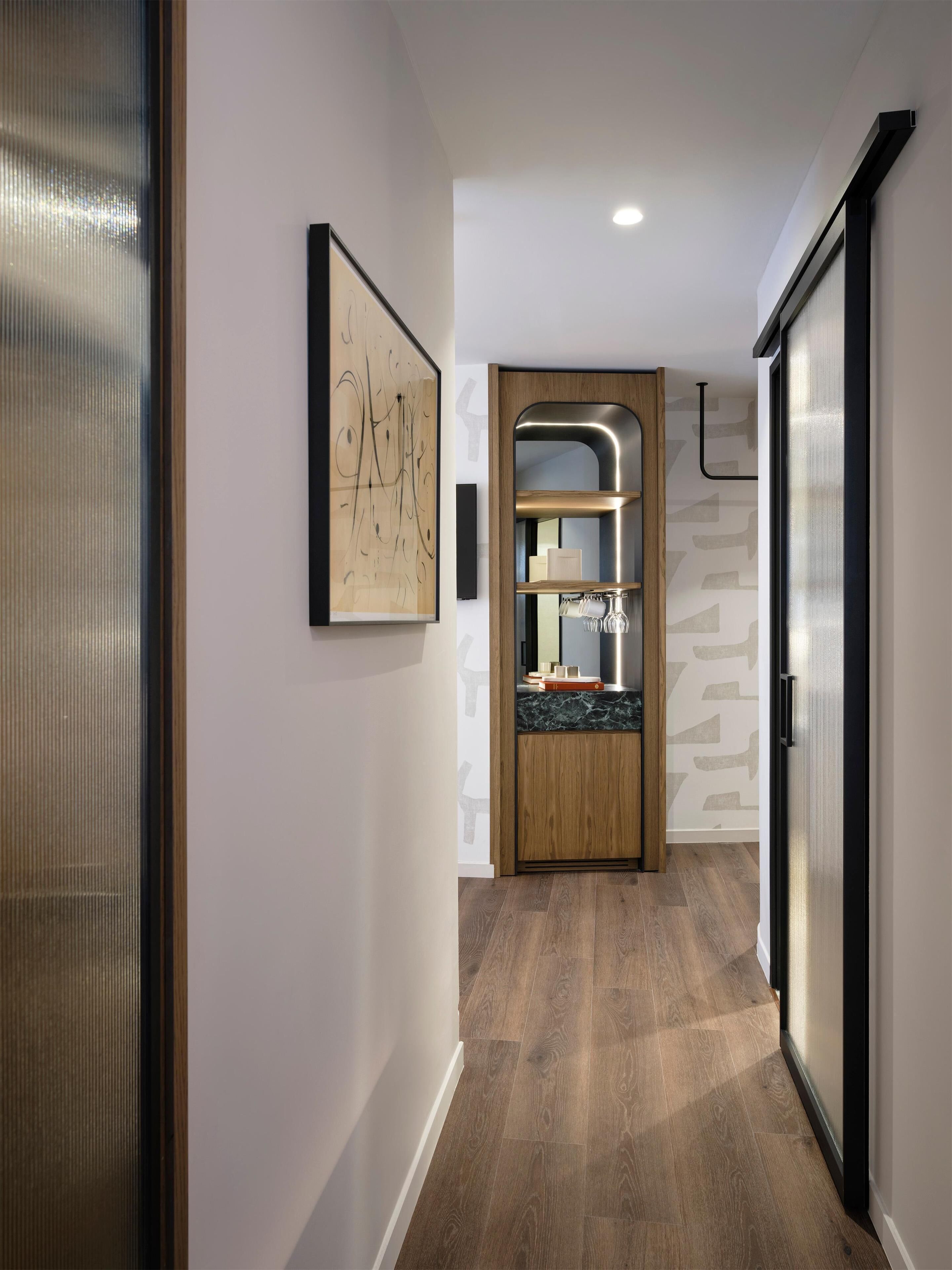 A hallway with a wooden door, a framed abstract painting, and a built-in shelf with glassware.