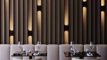 A modern dining area with two tables, each with a glass and a wine glass, set against a wall with vertical panels and recessed lighting.