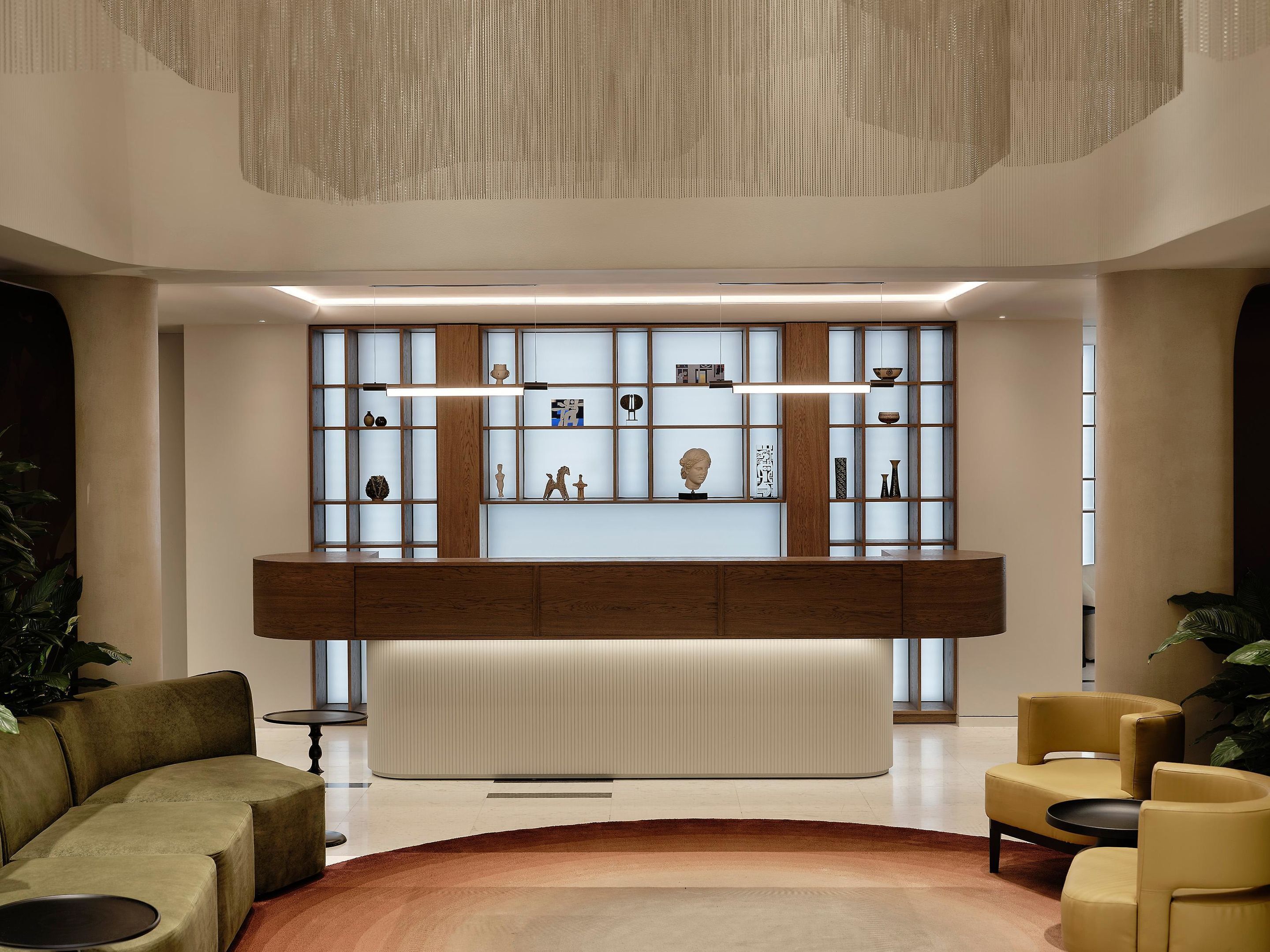 A modern lobby with a central reception desk, seating area, and decorative shelves.