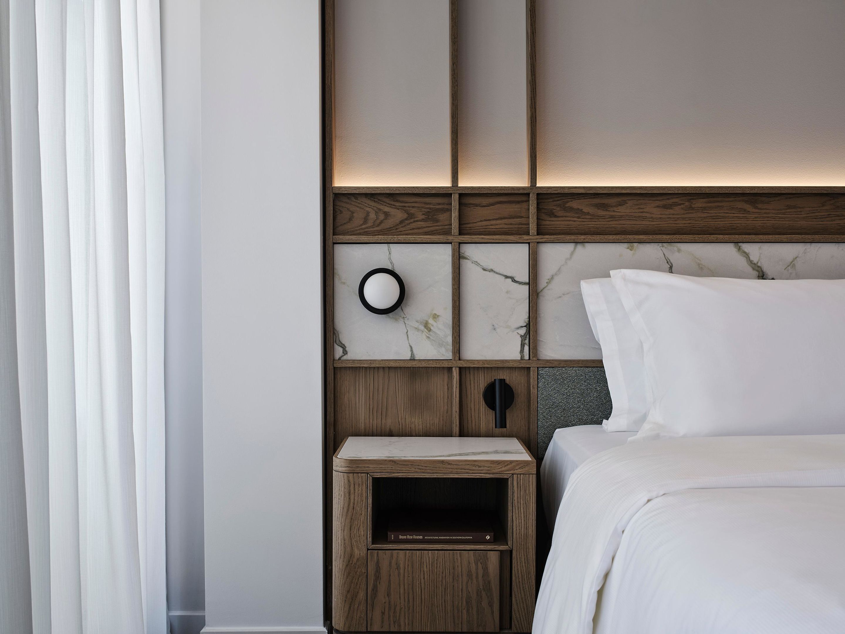 A hotel room with a bed, a nightstand, a wall-mounted light, and a marble-patterned headboard.