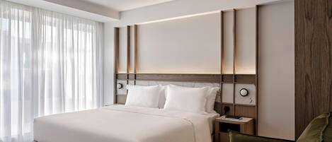 Et moderne hotelværelse med en stor seng, et træhovedgærde, et natbord med lampe og en grøn lænestol.