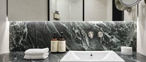 A bathroom with a marble countertop, two Nuxe skincare bottles, a white sink, and a mirror.