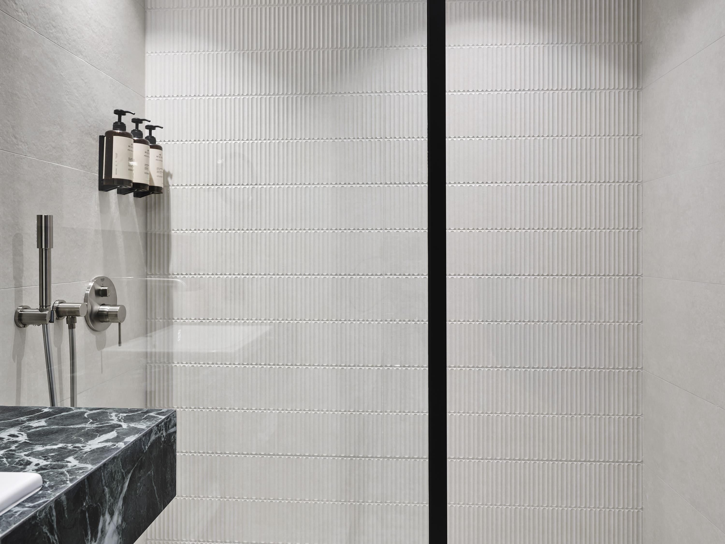 A modern bathroom with a marble countertop, a shower with a handheld showerhead, and a vertical black stripe on the wall.