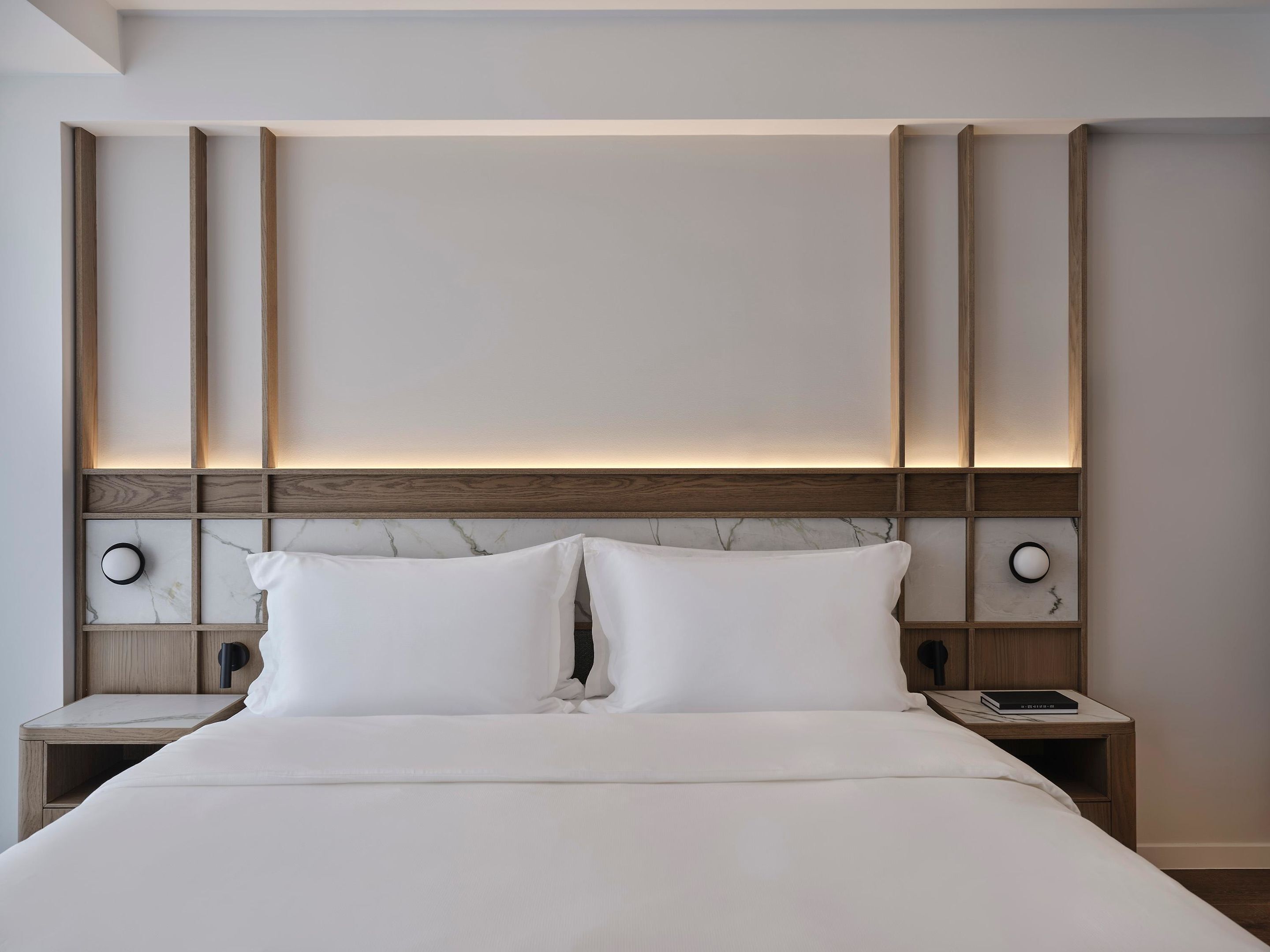 A modern bedroom with a large bed, wooden headboard, bedside tables, and a nightstand.