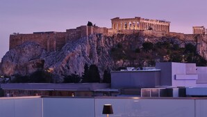 A rooftop restaurant with tables set for dining, overlooking a historic building on a cliff.