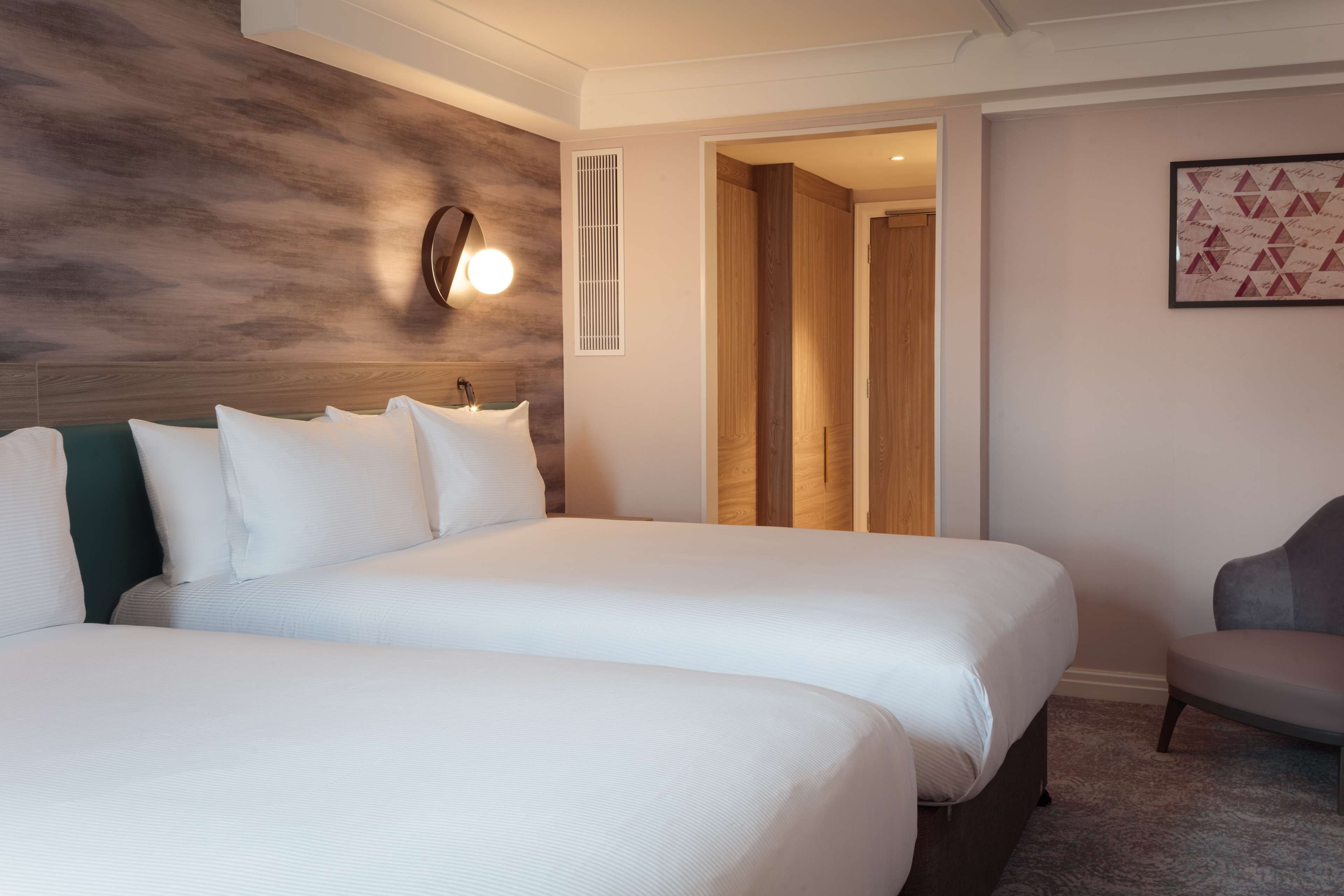 A hotel room with two beds, a sitting area, and a view of the hallway.